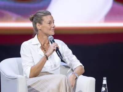 Female speaker addressing the audience during a panel at NGSC, seated and holding a microphone